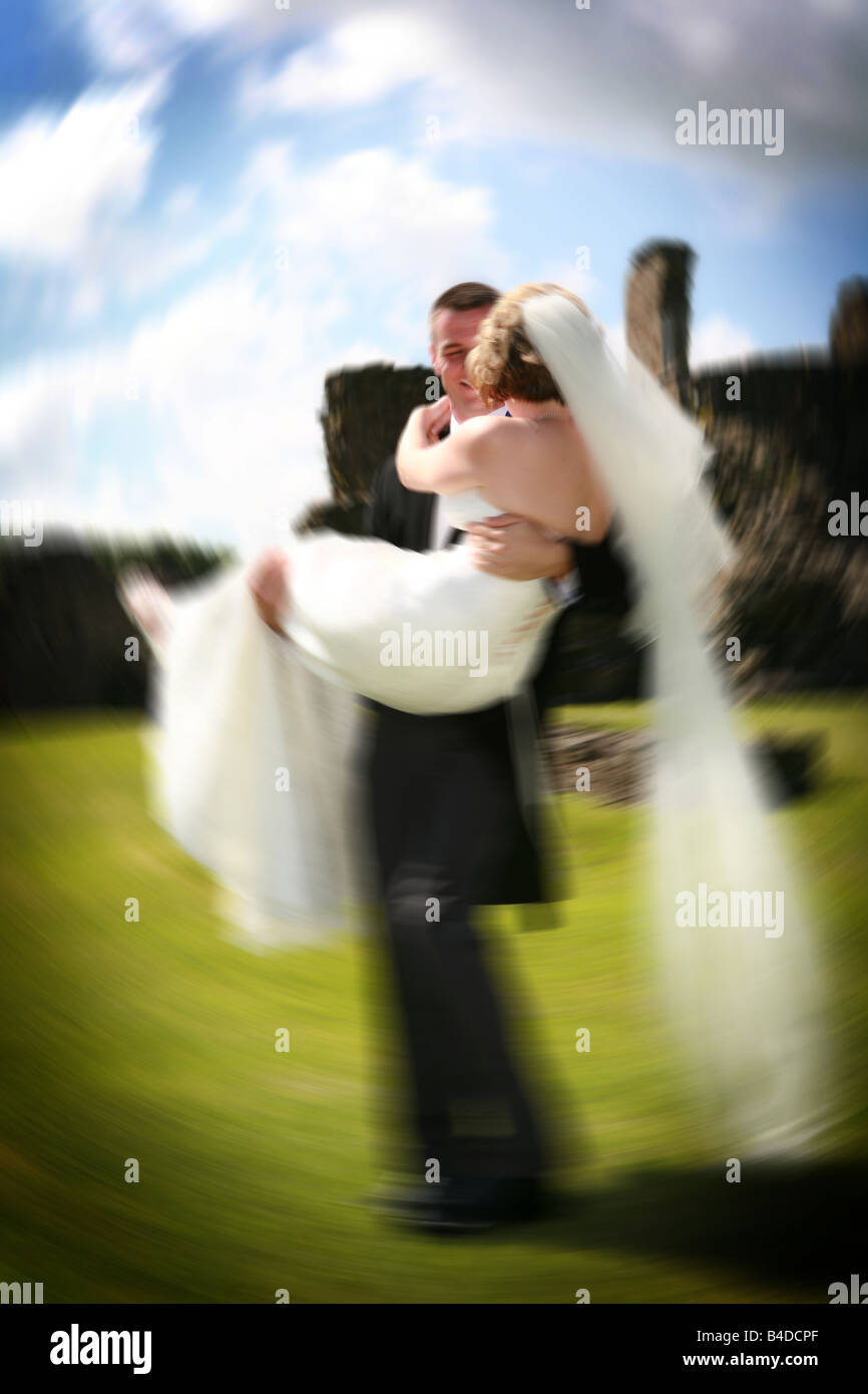 Lo sposo holding sposa in armi in bianco abito da sposa gira intorno sul giorno di nozze una contemporanea matrimonio foto divertente sensazione felice Foto Stock