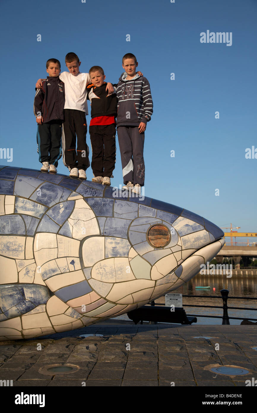 Bambini locali giocare sul grande pesce Salmone scultura di Giovanni gentilezza accanto al fiume Lagan in Belfast City Centre Foto Stock