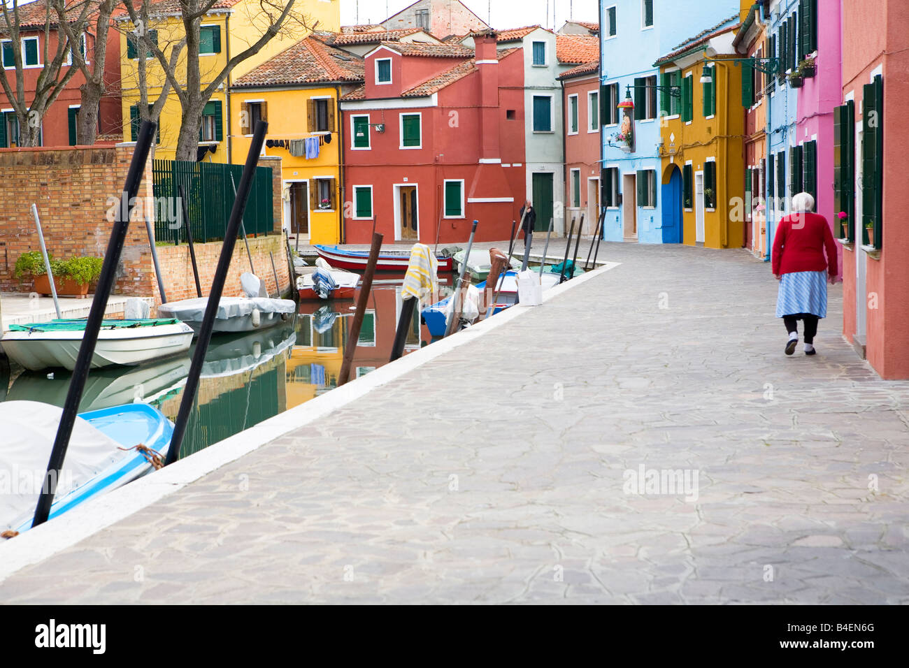 Donna matura cammina giù per una strada multicolore su isola di Burano Venezia Italia Foto Stock