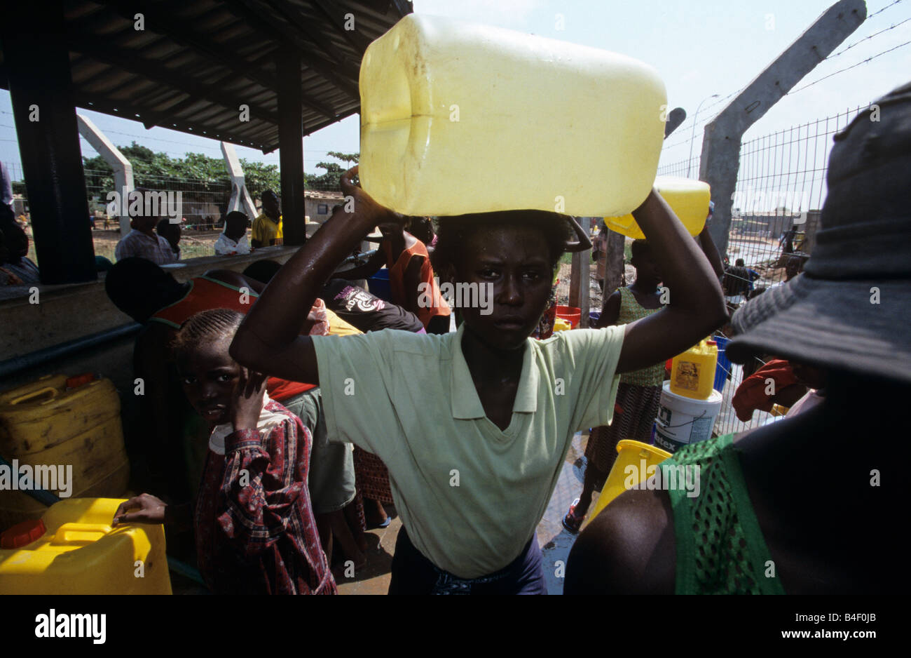 Donna che trasportano jerry può sulla testa, tra gli altri la raccolta di acqua in sfollati camp, Angola Foto Stock