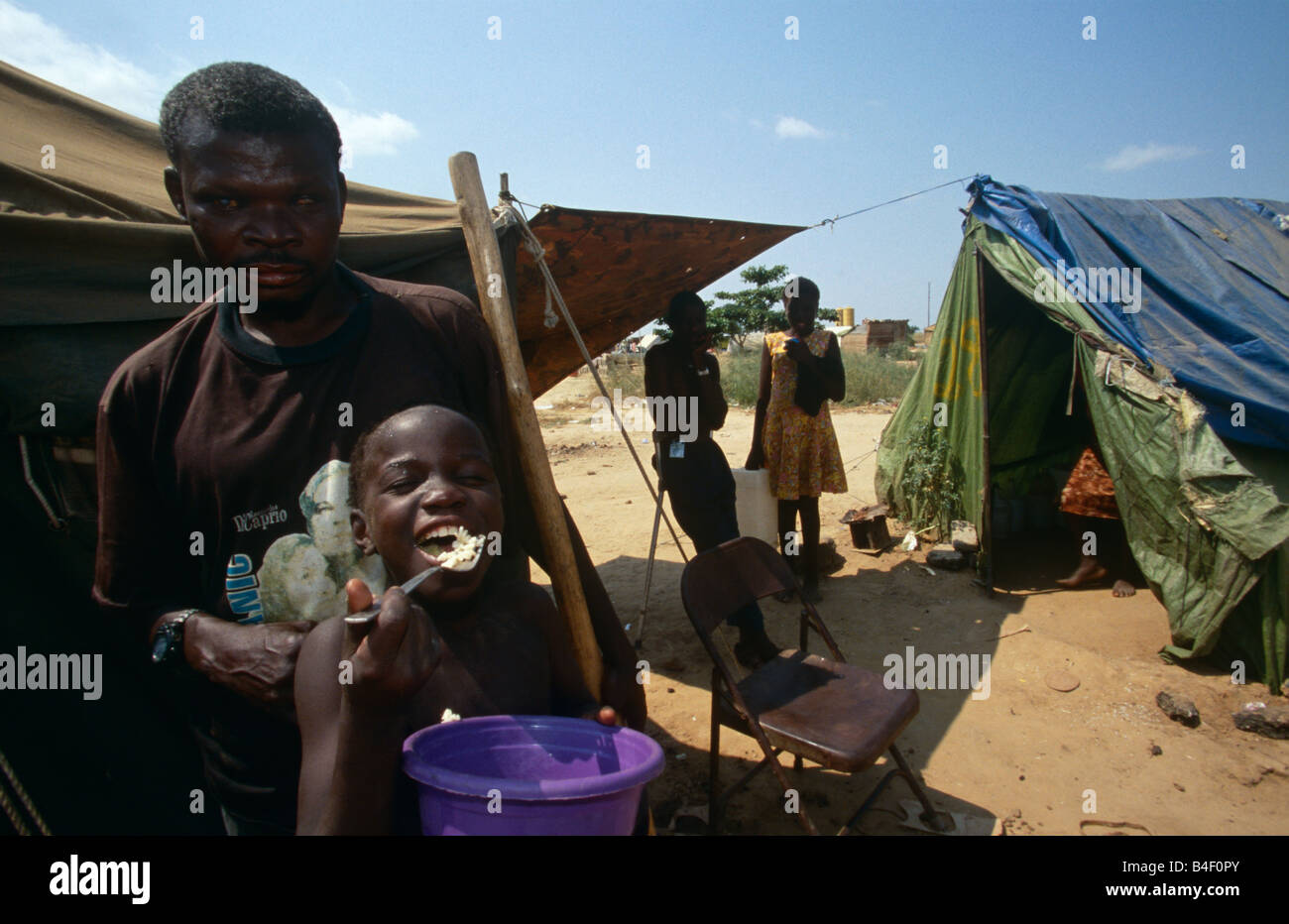 Felice ragazzo con cibo tra sfollati e tende a camp, Angola Foto Stock