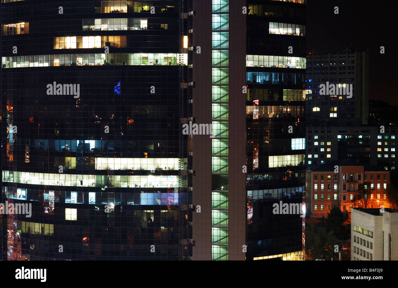 Shining torre del grattacielo contro la città di notte, la piazza e le finestre rettangolari running light Foto Stock