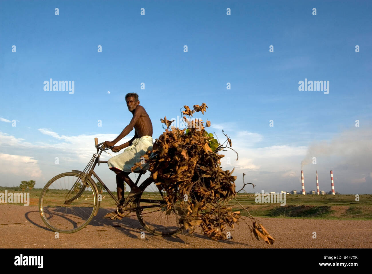 Una persona anziana dal villaggio di foglie portante nel suo ciclo nella parte anteriore di un 3x210 MW di potenza termica impianto nel Bengala occidentale,l'India Foto Stock