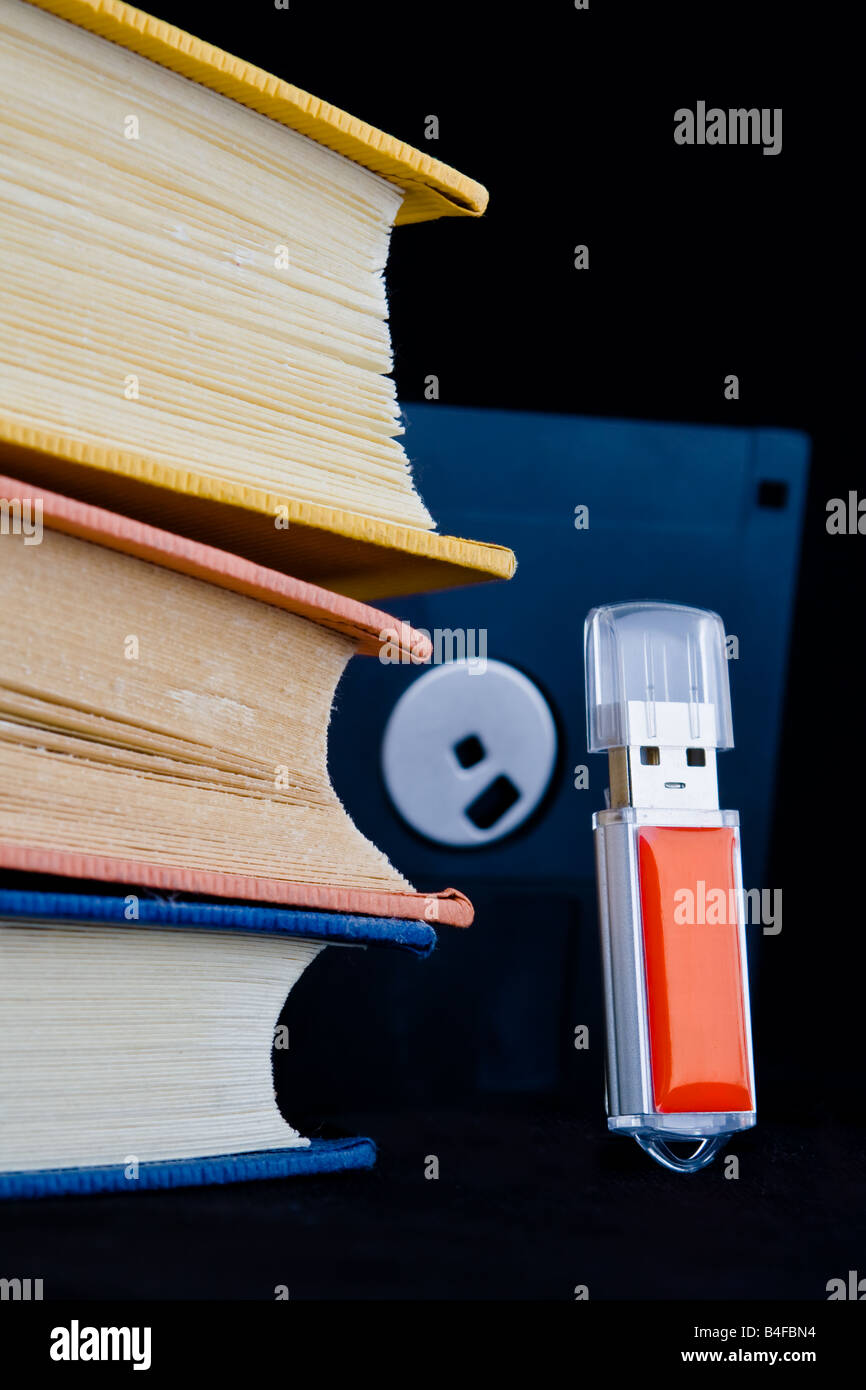 Tre libri e un floppy disk telaio minacciosamente su un rosso chiave usb in posizione eretta; i vecchi media vorrebbe vendicarsi sui nuovi supporti digitali Foto Stock