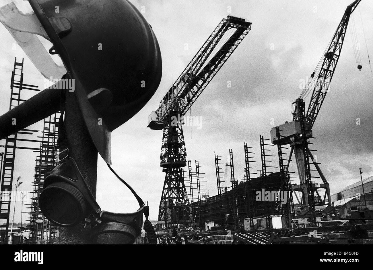 Un casco appeso con i saldatori occhiale tra le gru a vuoto dopo la chiusura dei cantieri navali Govan cantiere in Scozia Agosto 1979 Foto Stock