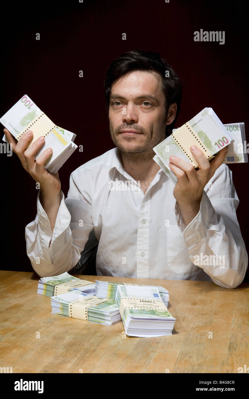 Un uomo seduto a un tavolo con fasci di centinaia di banconote in euro Foto Stock