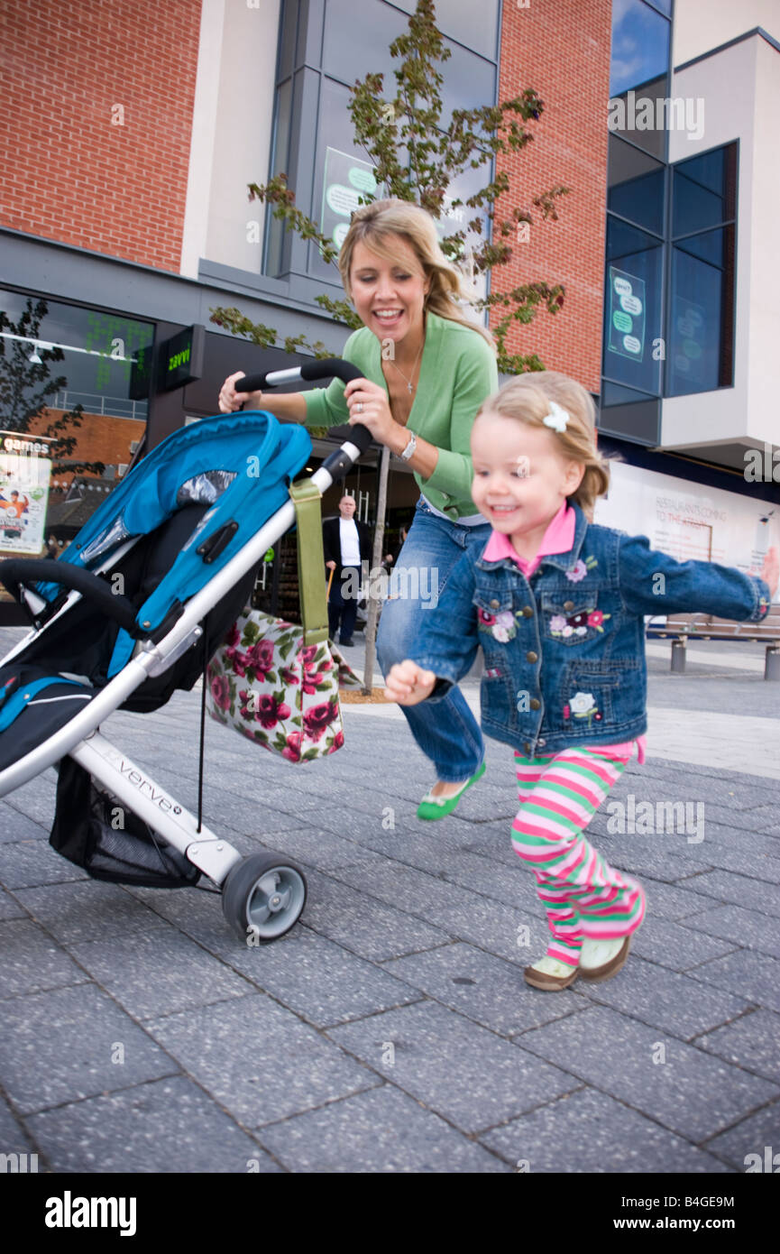 Madre di spingere un passeggino con la sua bambina racing insieme al suo fianco Foto Stock