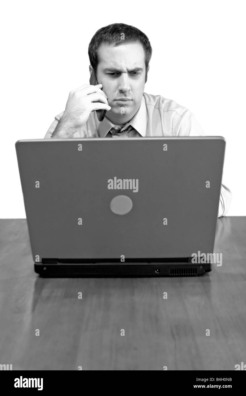 Un uomo che lavora da casa con il suo telefono cellulare e il computer portatile in bianco e nero ha una alterazione o prendere sul serio sul suo volto Foto Stock