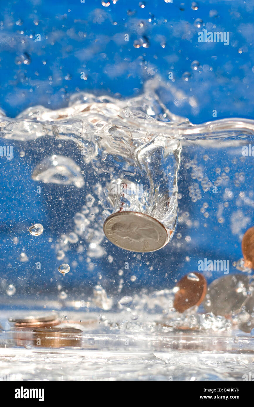 Una manciata di monete che cade in una piscina di acqua Foto Stock