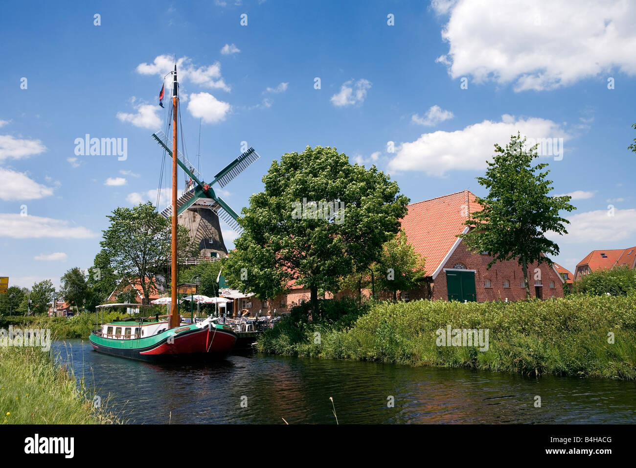 Barca a vela in canal con il mulino a vento di industriale in background Ostgrossefehn Bassa Sassonia Germania Foto Stock