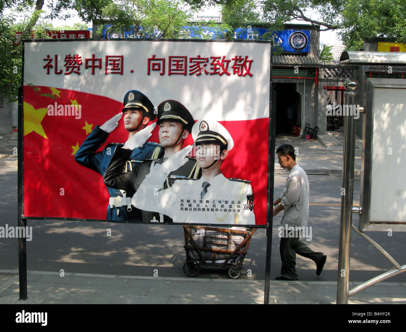 Un Cinese passeggiate nativo passato un cartellone che mostra di polizia e militari che plaude a Pechino in Cina Foto Stock