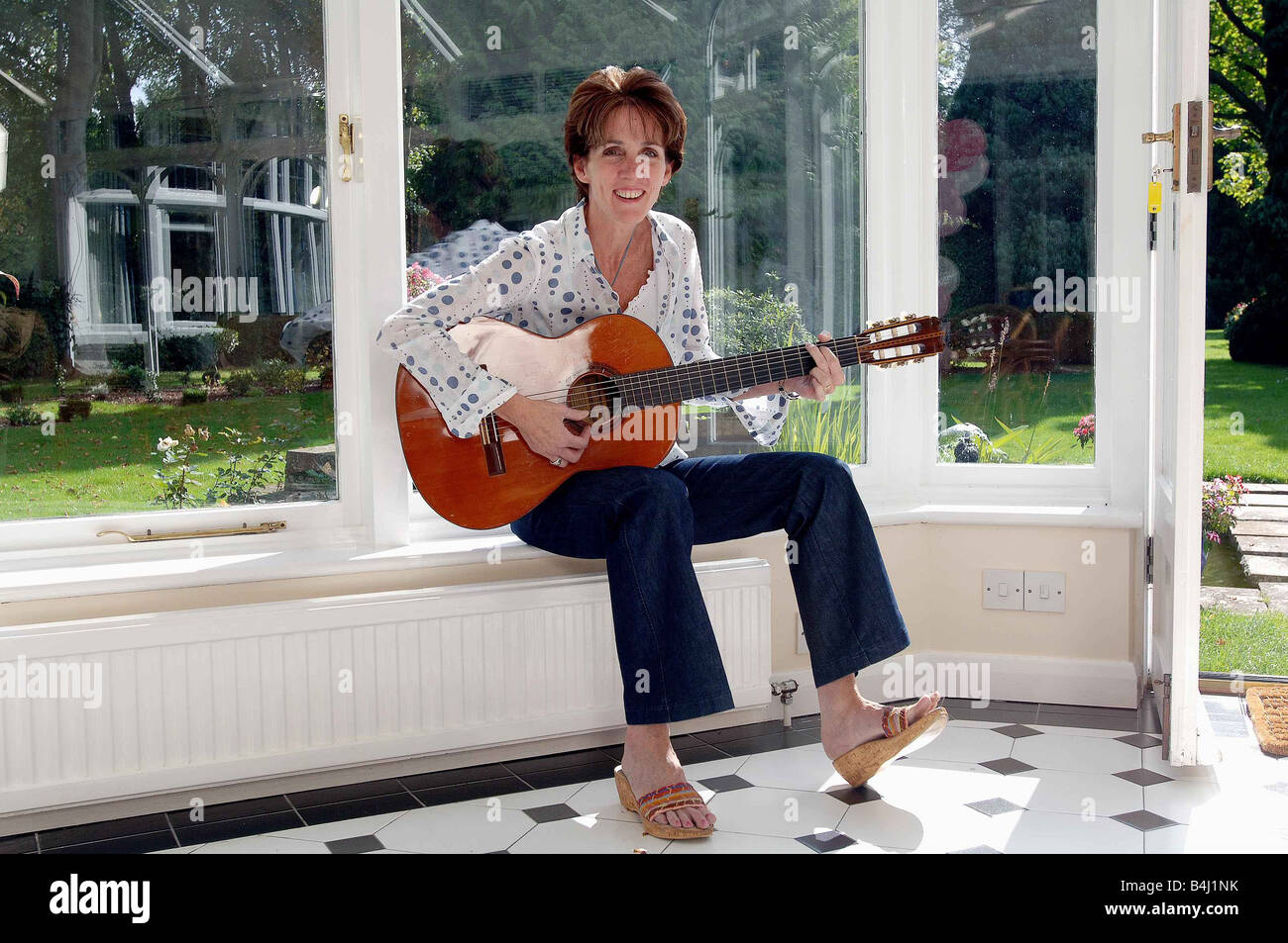 Eileen Rossi moglie di Status Quo rocker Francesco Rossi presso la casa di famiglia in Purley seduti a casa a suonare la chitarra rilassante in una poltrona Foto Stock