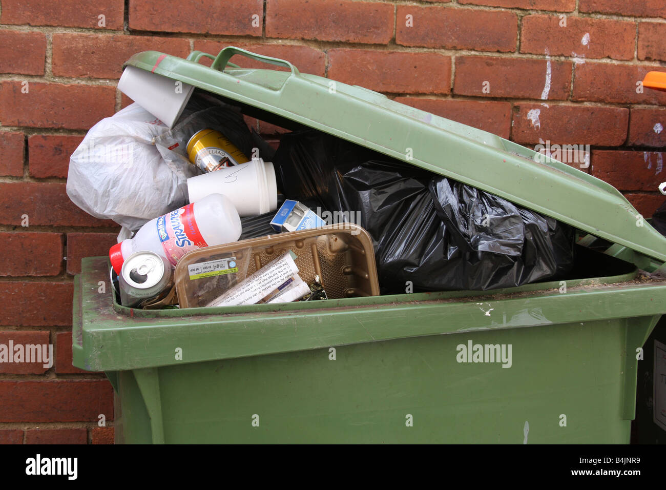 Tipo di ruote bidone dei rifiuti oltre riempito di rifiuti e rifiuti con il coperchio parzialmente aperto. Foto Stock