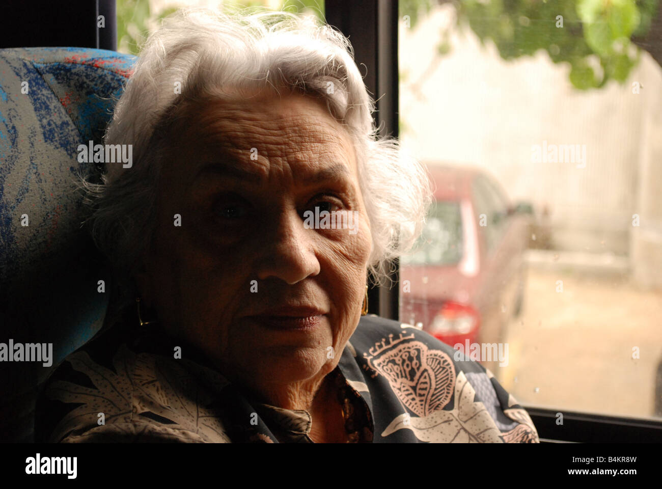 Una nonna, dei capelli bianchi, guarda dritto mentre si attende per il suo prossimo destino. Foto Stock