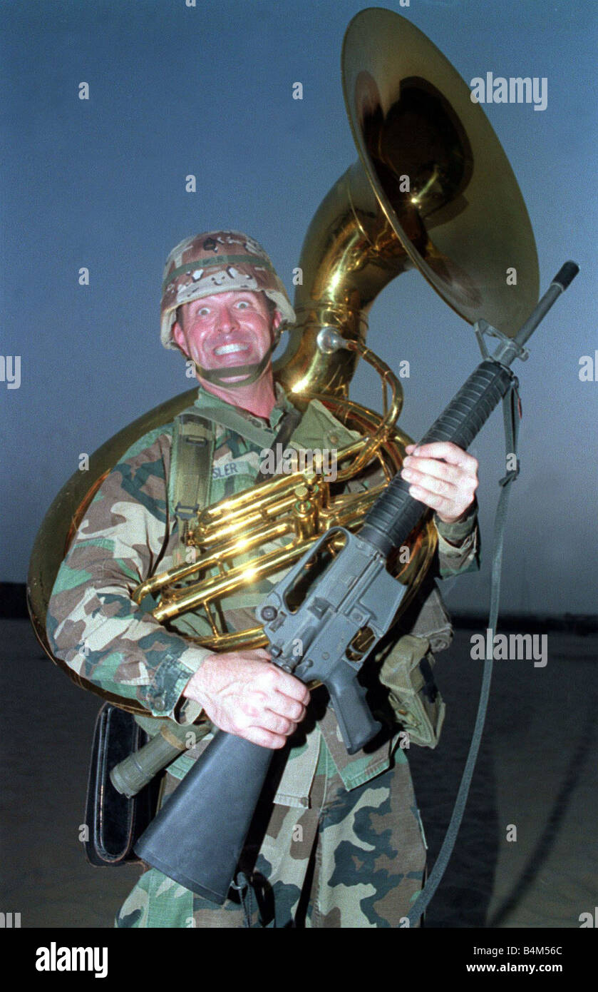 Guerra del Golfo la tempesta di deserto di funzionamento soldato americano tenendo la mitragliatrice e indossando un sousaphone come se il suo combattimento normale wasn ingranaggio Foto Stock