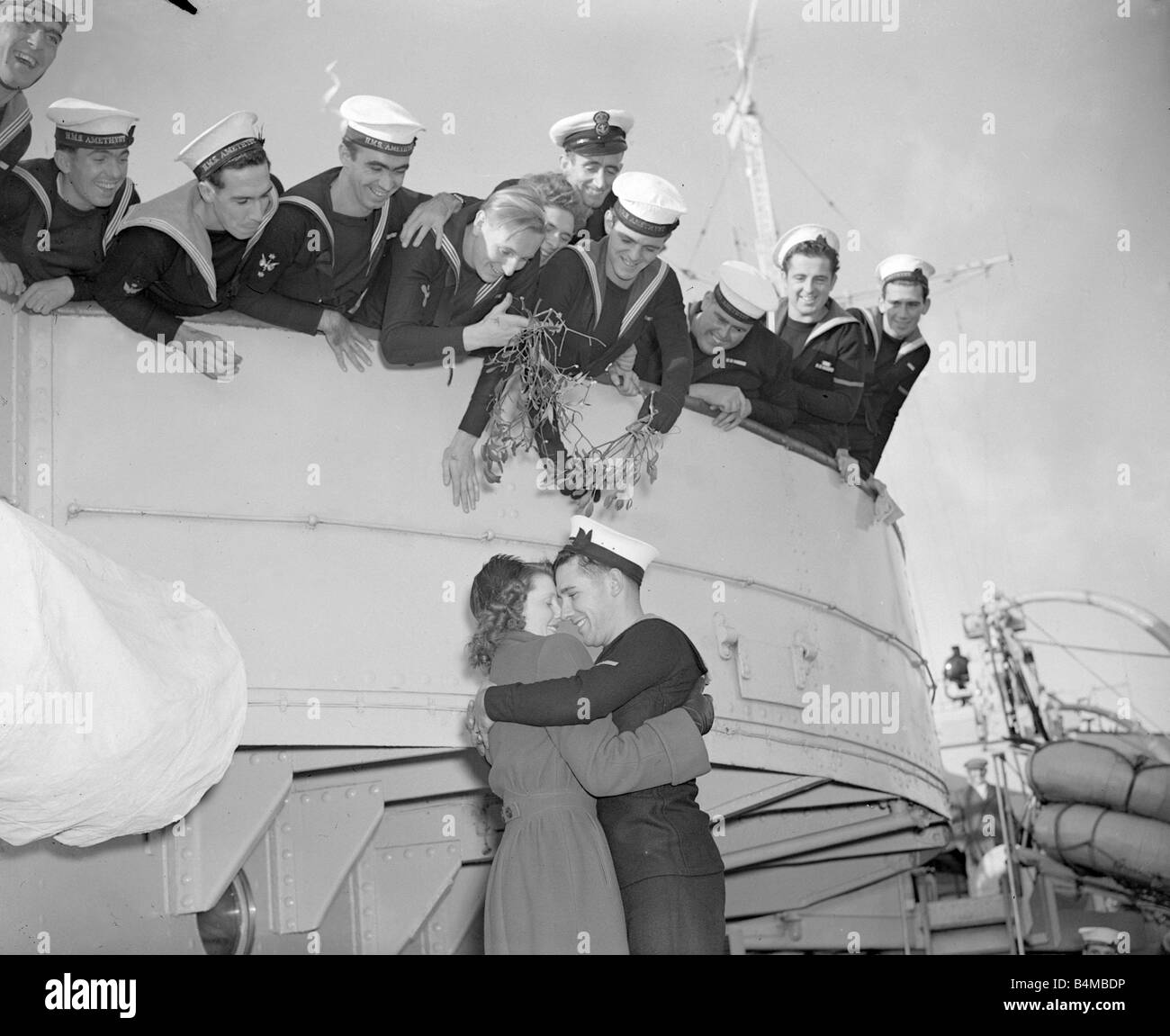 John Webber di HMS Amethyst riunisce con sua moglie Maria e le conferisce un abbraccio il suo shipmates ridere tenere una barch di vischio sopra le loro teste Foto Stock