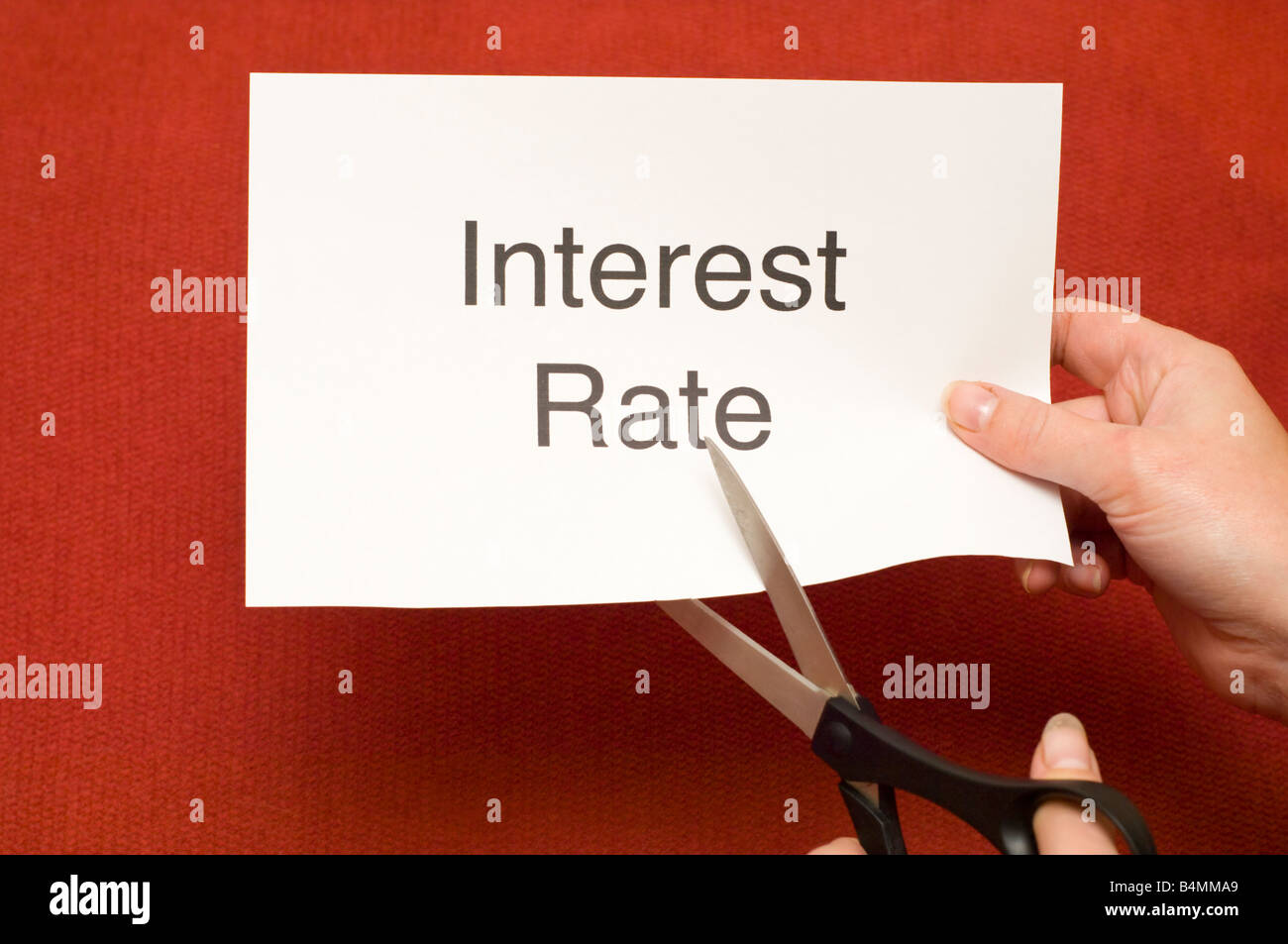 Immagine di persona il taglio di un pezzo di carta con "tasso di interesse" scritto su di esso utilizzando un paio di forbici Foto Stock