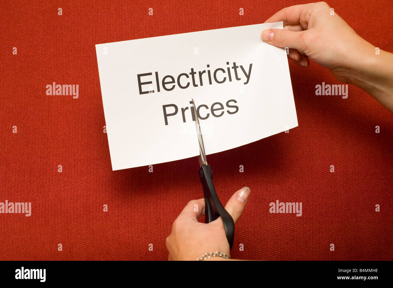 Immagine di persona il taglio di un pezzo di carta con "l'elettricità prezzi " scritto su di esso utilizzando un paio di forbici Foto Stock