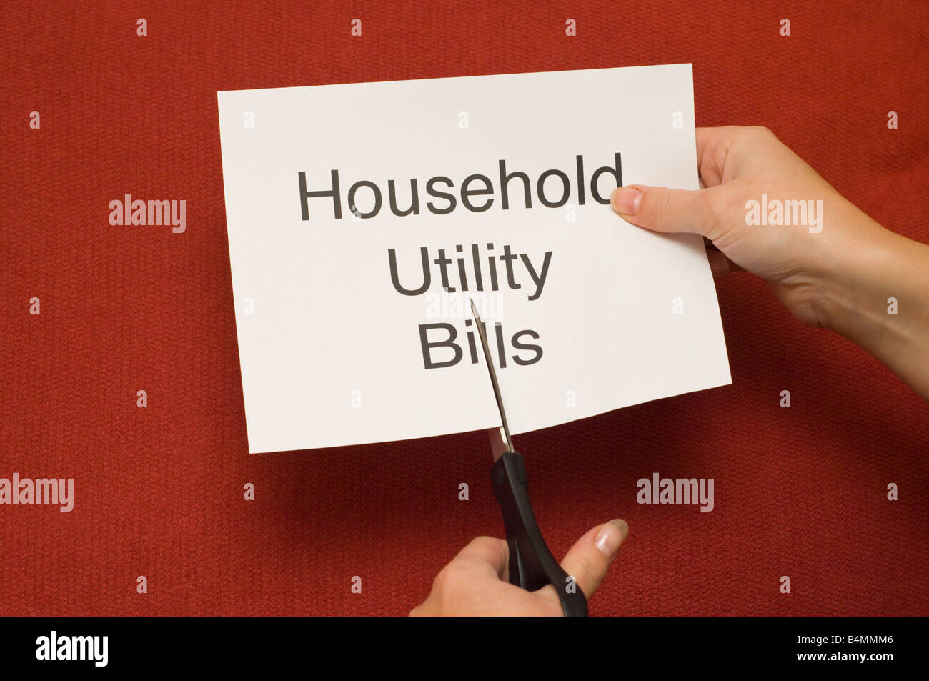 Immagine di persona il taglio di un pezzo di carta con "Famiglia bollette' scritto su di esso utilizzando un paio di forbici Foto Stock