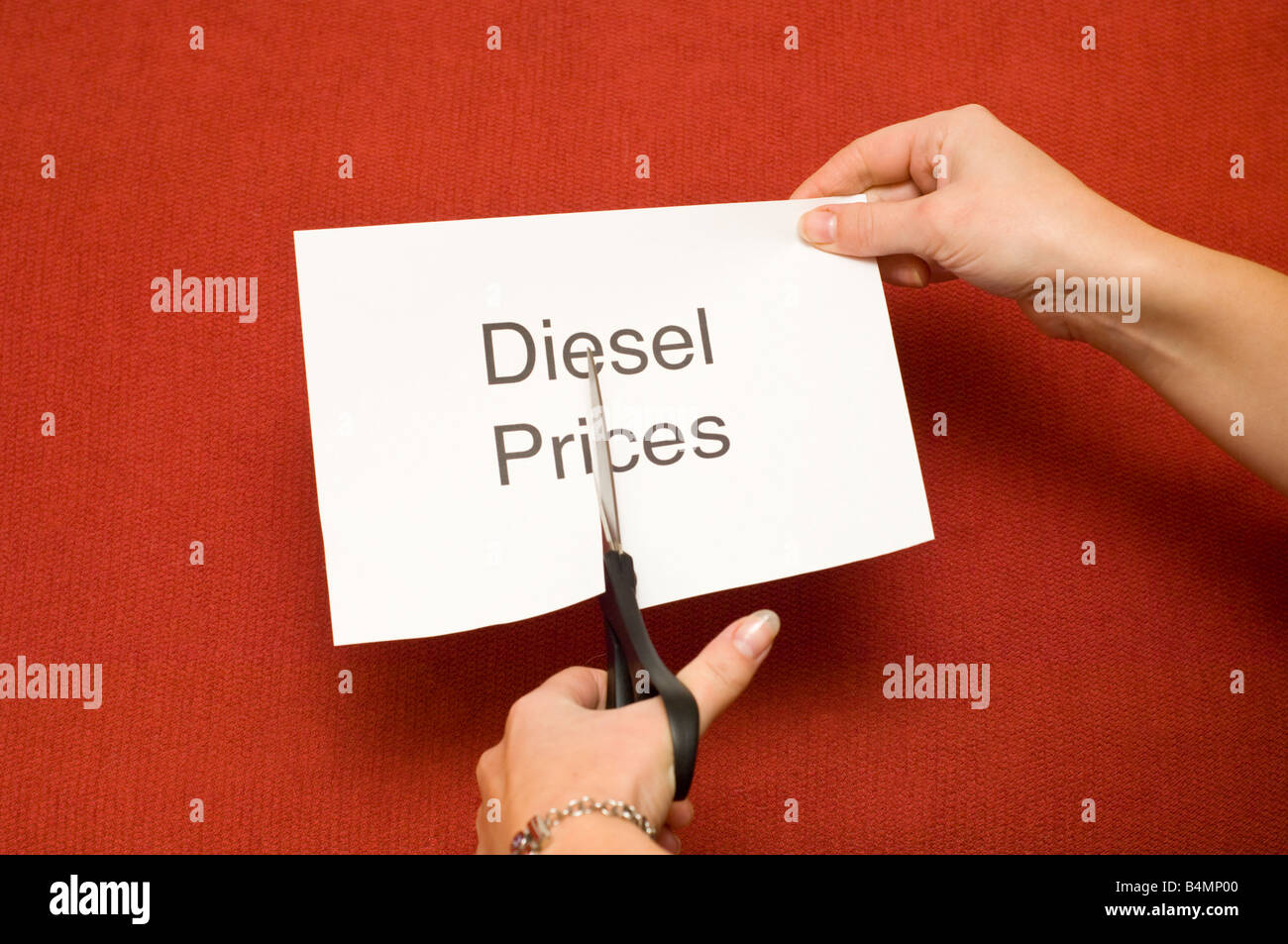 Immagine di persona il taglio di un pezzo di carta con 'Diesel' prezzi scritti su di esso utilizzando un paio di forbici Foto Stock