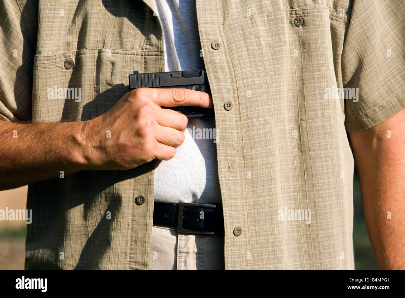 Un uomo tira una pistola nascosta arma fuori dalla sua maglietta. Foto Stock