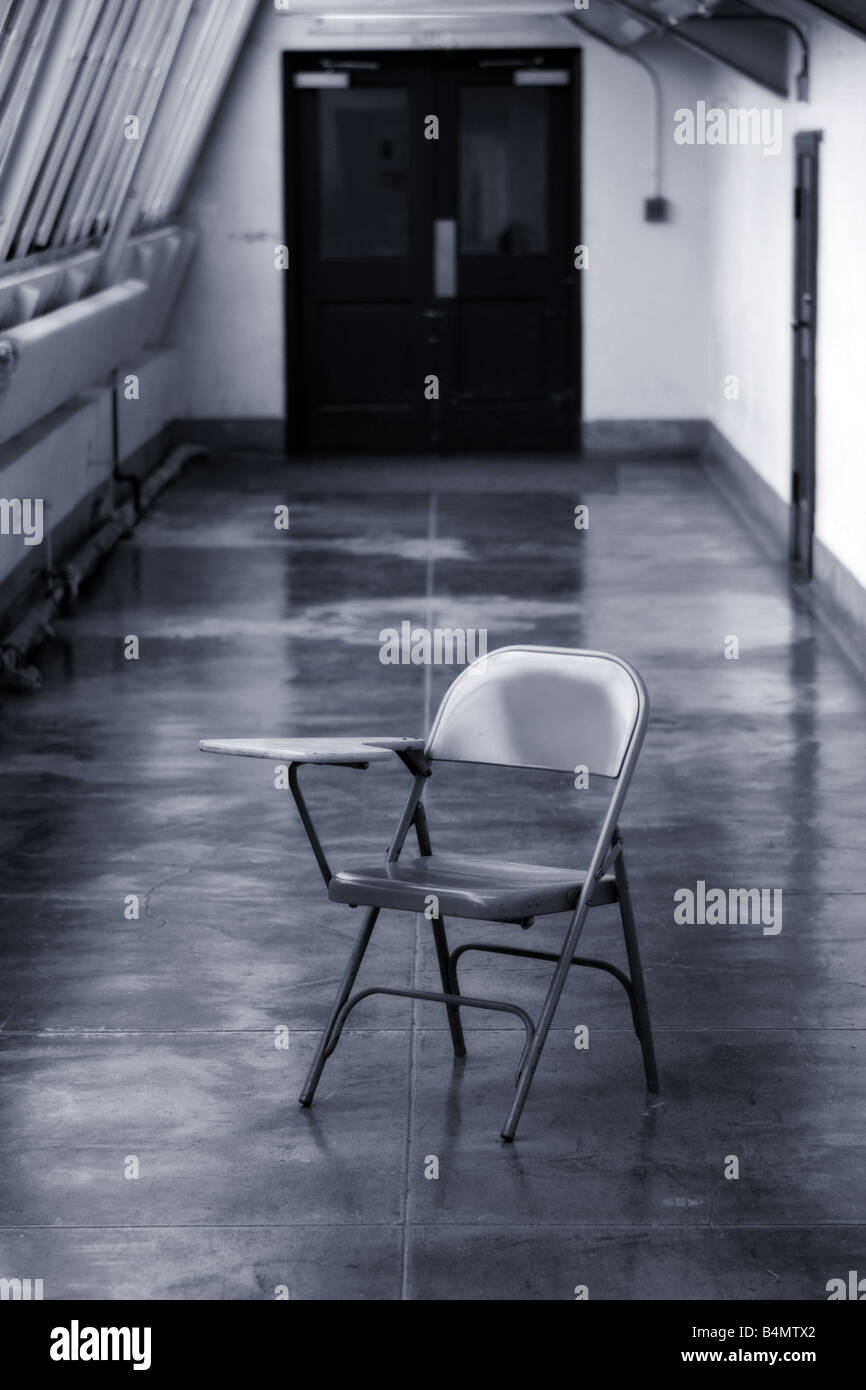 Una scuola sedia scrivania si siede in un lungo corridoio Foto Stock