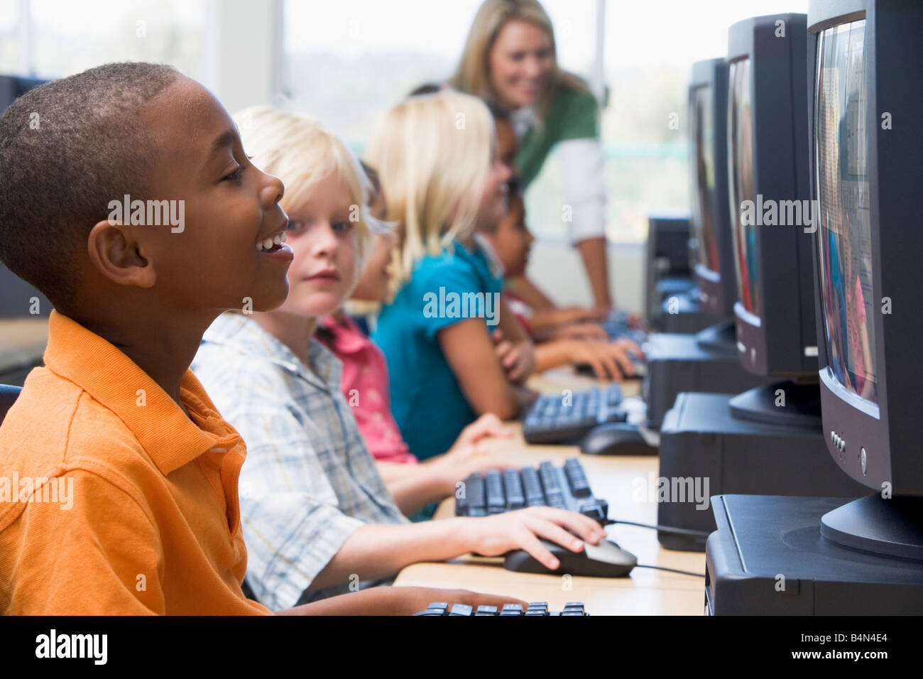 Sei bambini in corrispondenza di terminali di computer con insegnante in background (profondità di campo/high key) Foto Stock