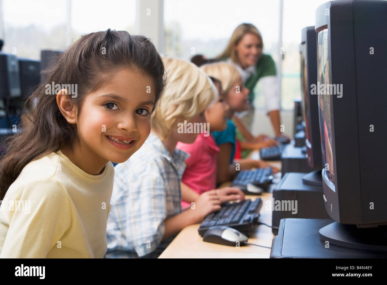 Bambini a terminali di computer con insegnante in background (profondità di campo/high key) Foto Stock