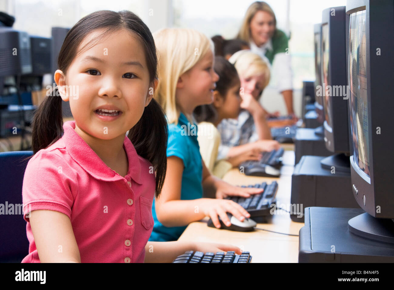 Bambini a terminali di computer con insegnante in background (profondità di campo/high key) Foto Stock