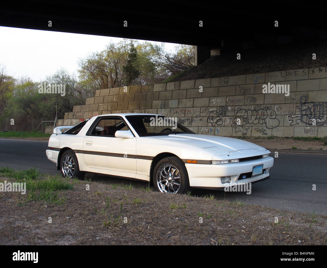 Un colpo di un bianco giapponese auto sportive al di sotto di una coperta di graffiti autostrada sopraelevata Foto Stock