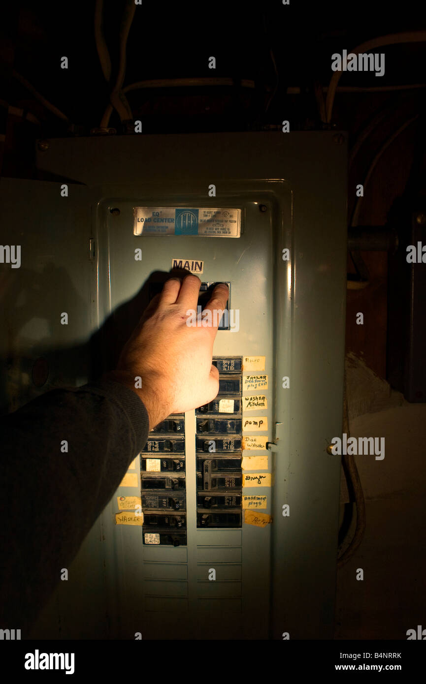 Una mano raggiunge per far scattare l'interruttore di circuito principale in una scatola interruttore illuminato con una luce flash. Foto Stock
