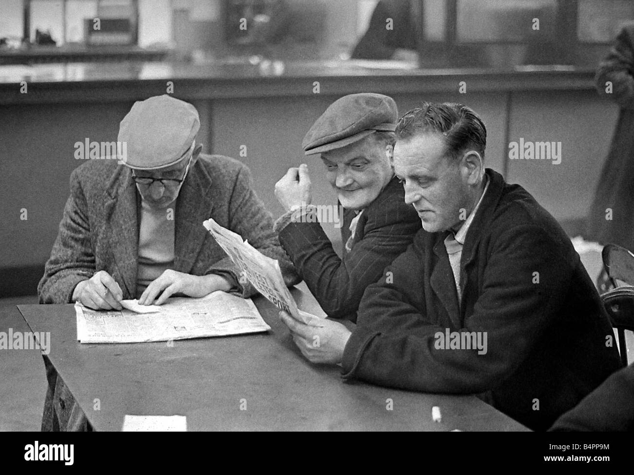 Uomini anziani studiare la forma guida prima di porre la loro scommessa in un negozio di scommesse Novembre 1962 Foto Stock
