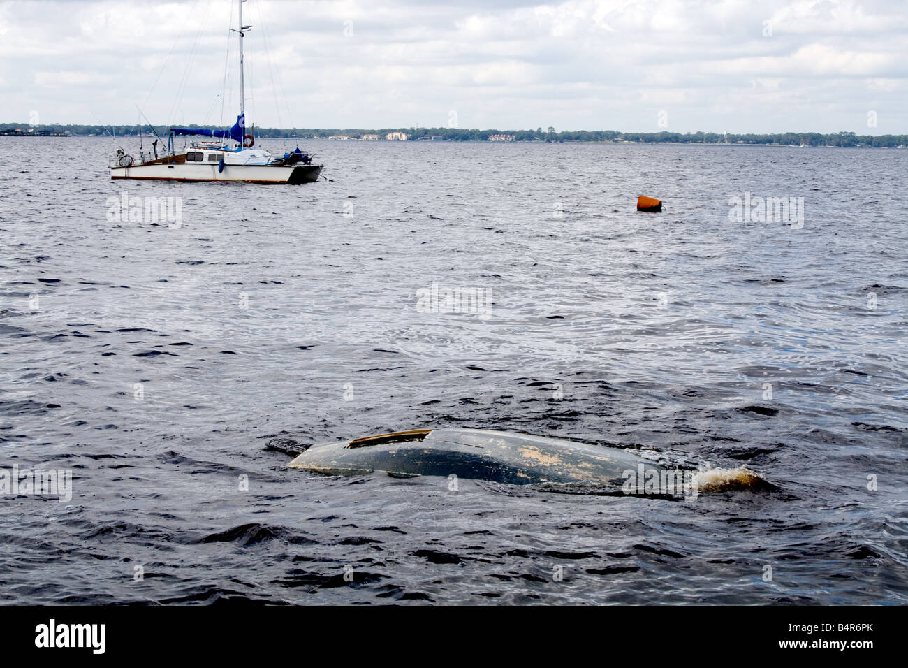 Fondo di una barca affondata quasi underwater sulle sponde di un lago con una piccola barca a vela in background Foto Stock