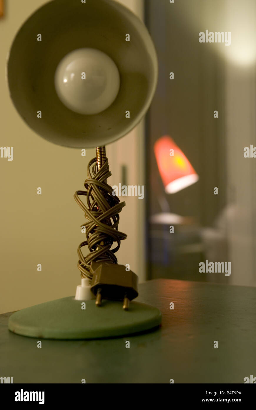 Dettaglio della lampada retrò sul tavolo con filo avvolto intorno il gambo e la luce rossa riflessa in background Foto Stock