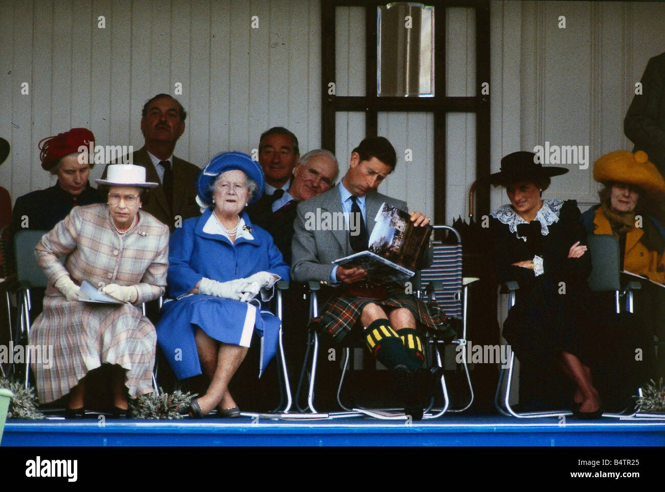 La regina Elisabetta 11 settembre leaing in avanti nella sua sede sul podio a Braemar Highland Games Regina madre guarda mentre il Principe Charles legge un libro guardato dalla Principessa Diana C T Roy Brit Regina Scozia n.8 Foto Stock
