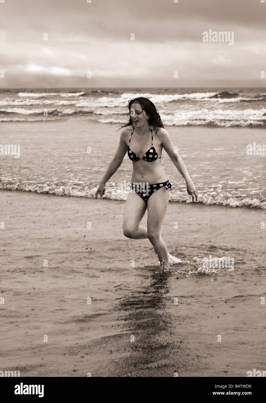 Giovane donna pagaiando sulla spiaggia sotto la pioggia Foto Stock