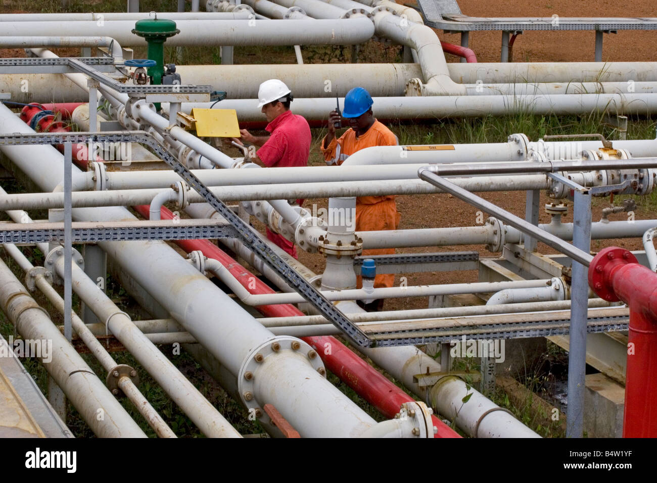 Olio Onshore impianto di lavorazione che mostra le tubazioni con olio ingegnere di produzione e assistente di effettuare interventi di manutenzione, il Gabon Foto Stock