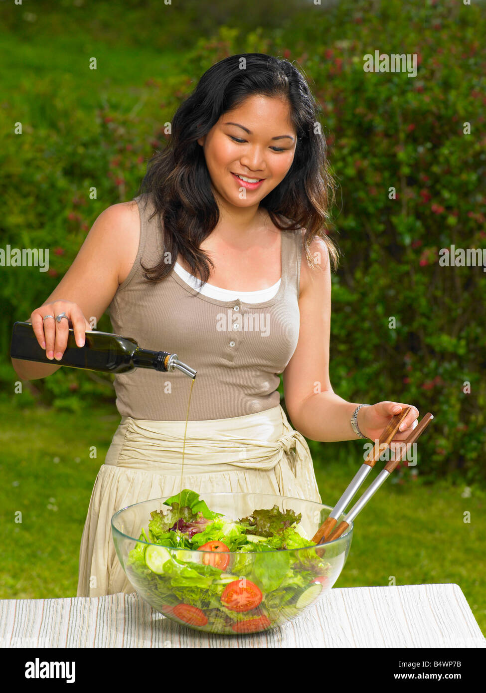 Giovane donna versando olio d'oliva su insalata Foto Stock