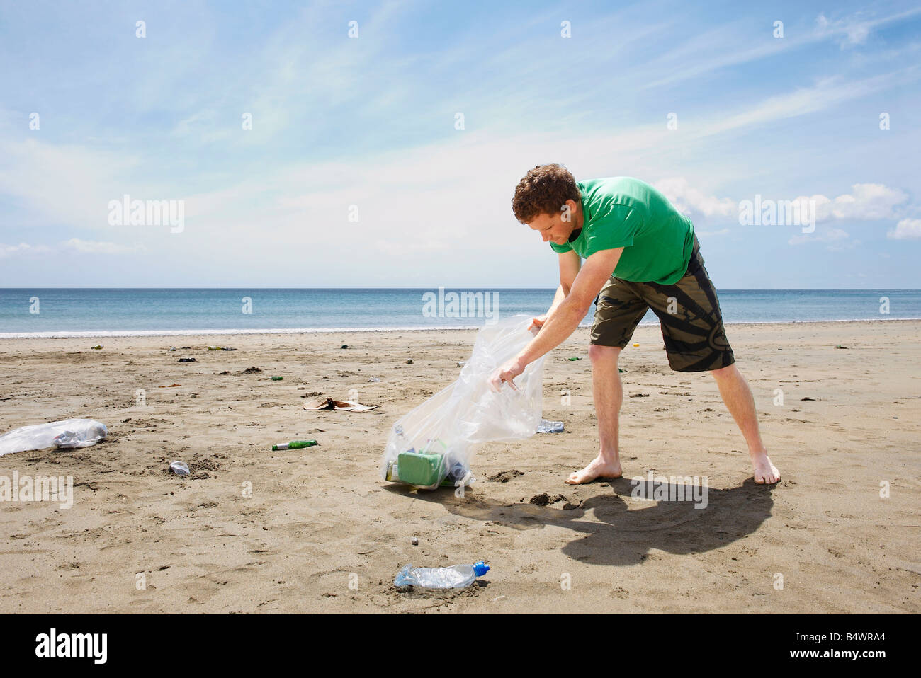 Giovane uomo raccogliere rifiuti sulla spiaggia Foto Stock
