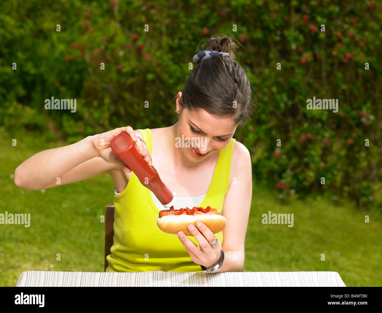Giovane donna versando il ketchup su hot dog Foto Stock
