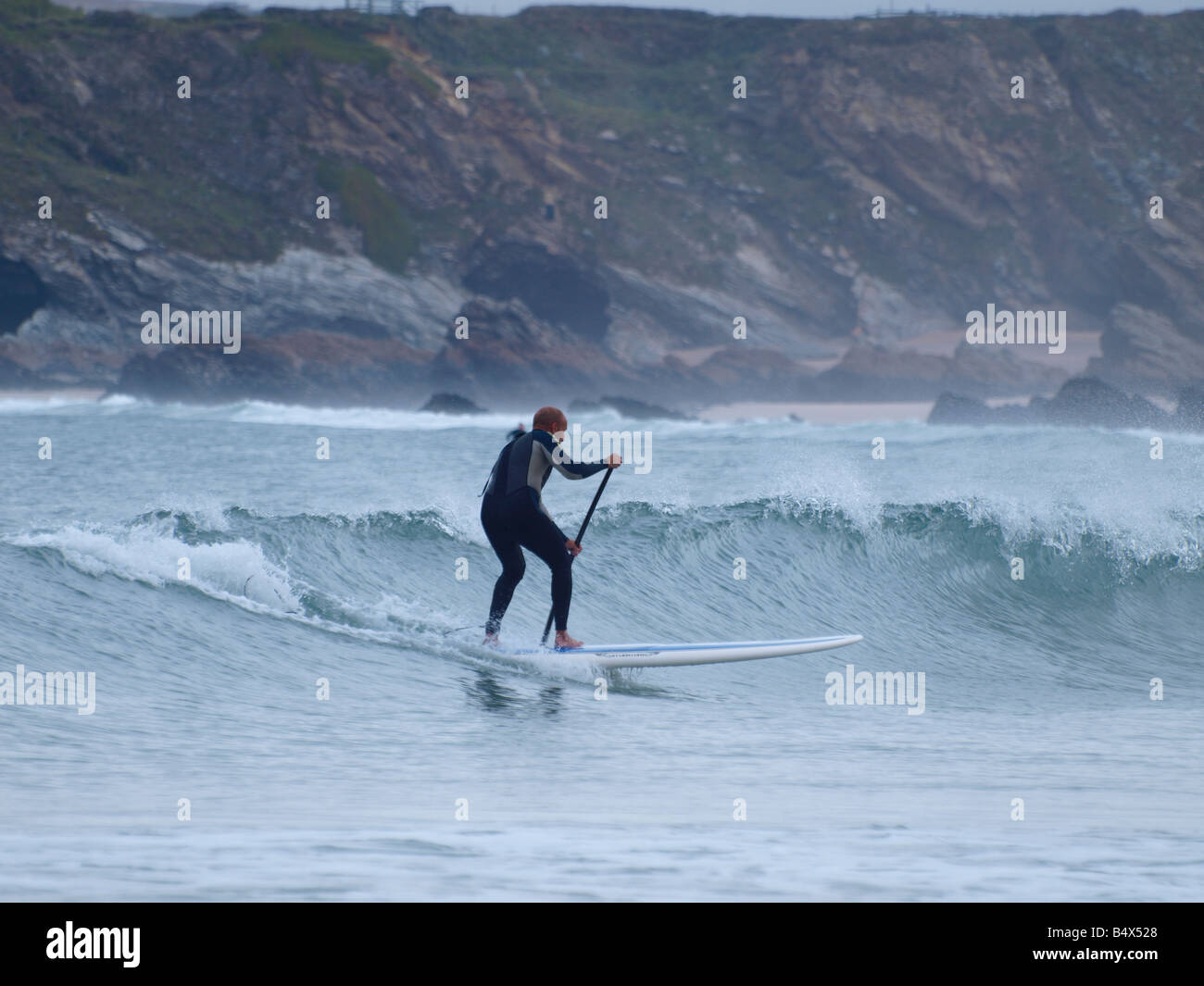 Un Stand Up Paddle Surfer cavalcare giù un'onda. Newquay, Cornwall Foto Stock