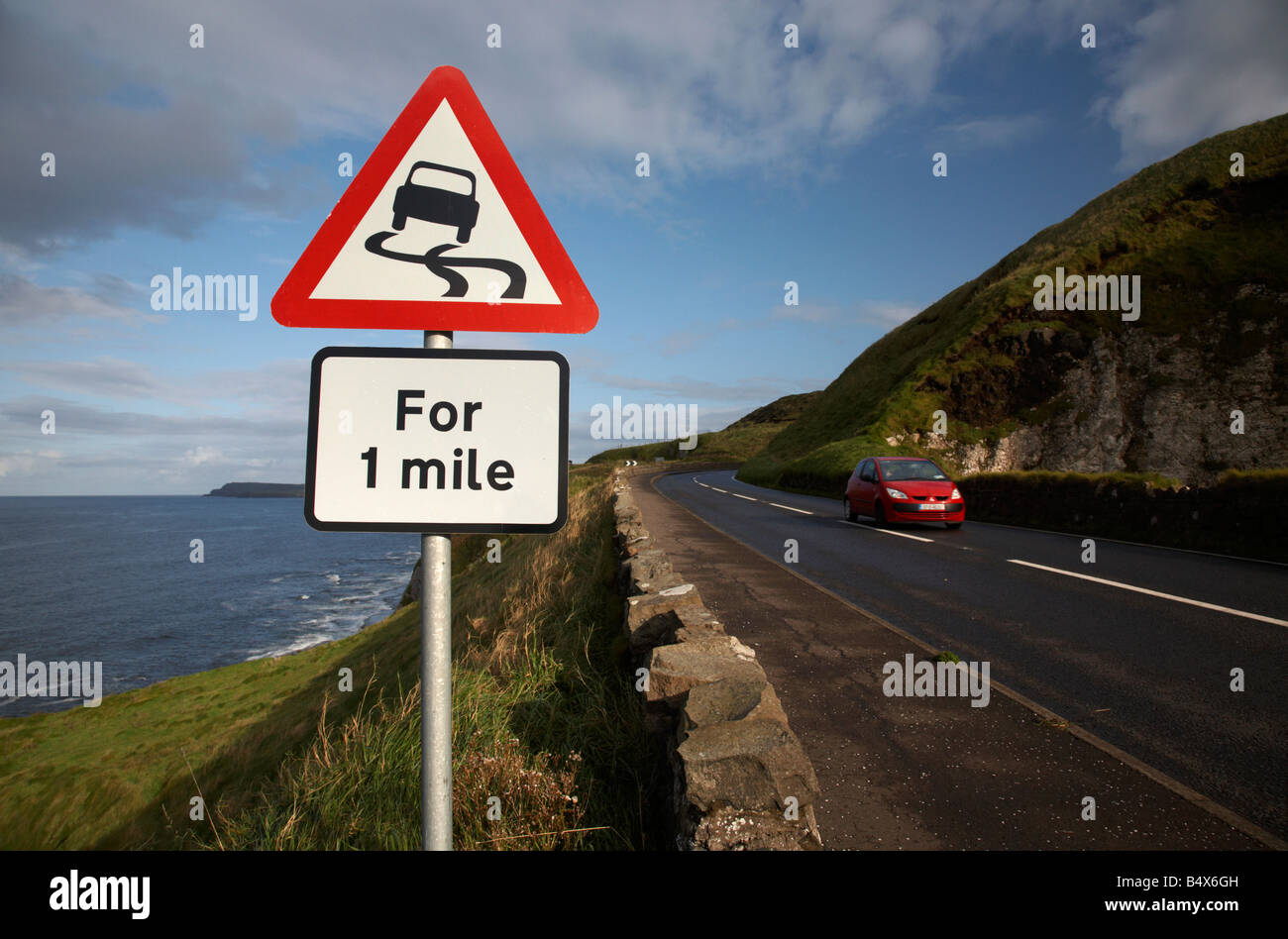 Automobile che viaggia oltre il fondo stradale sdrucciolevole pericolo rosso triangolo di avvertimento per 1 miglio segno sulla famosa A2 North Antrim causeway coastal Foto Stock