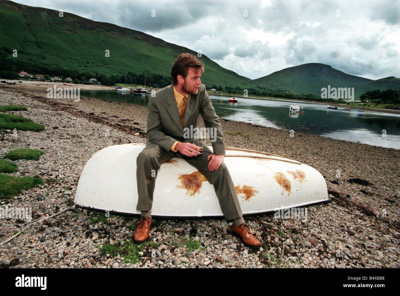 Ewan McGregor sull'isola di Arran Luglio 1998 con bottiglia di Loch Ranza single malt whisky seduto sulla barca capovolta Foto Stock