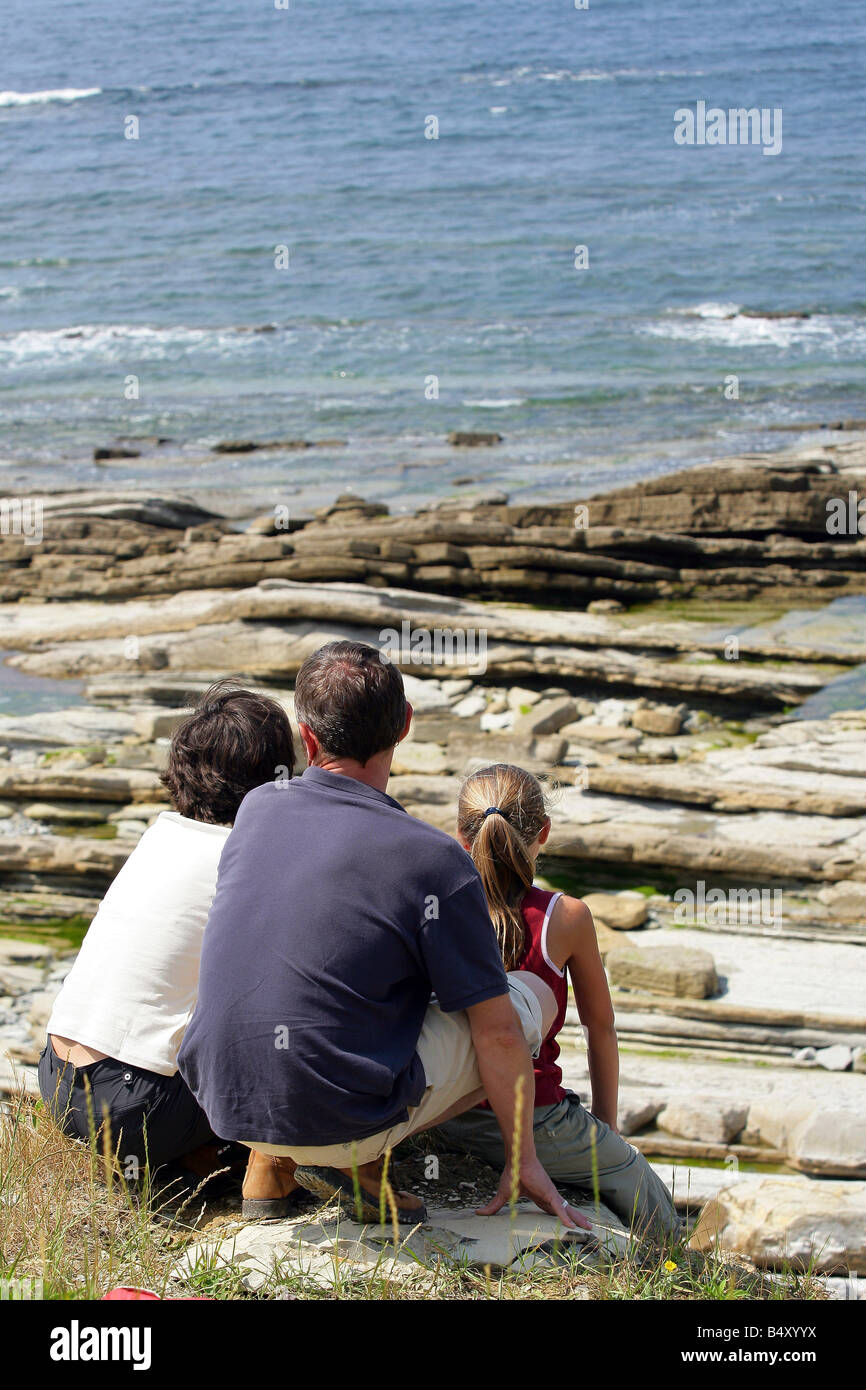 Famiglia seduti sulle rocce guardando il mare, vista posteriore Foto Stock