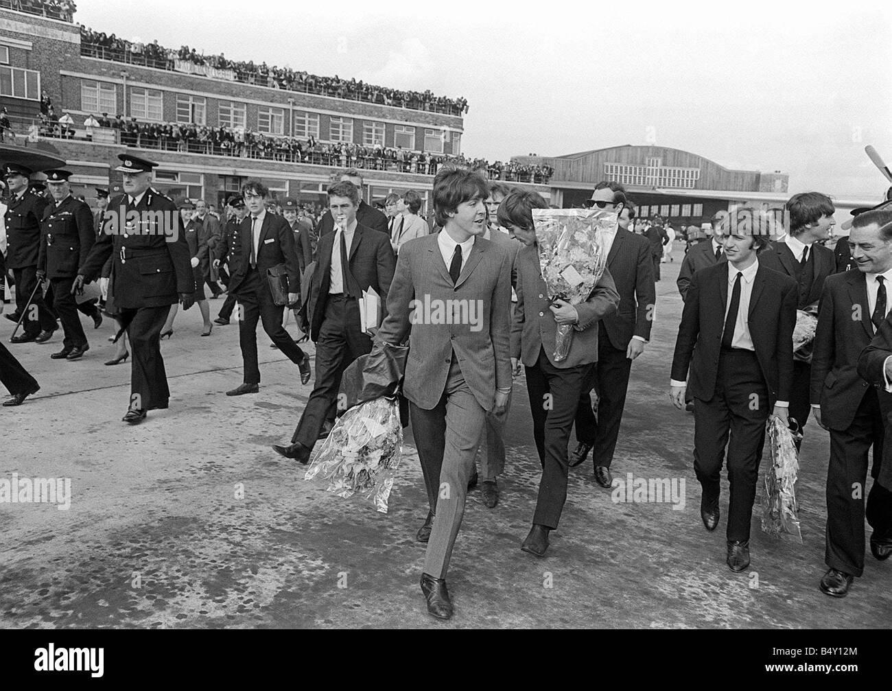 Gruppo pop The Beatles Luglio 1964 John Lennon Paul McCartney George Harrison Ringo Starr dei Beatles in Liverpool arrivano all'Aeroporto di Liverpool per la premiere del nord di una dura giornata s notte azienda bouquet di fiori Foto Stock