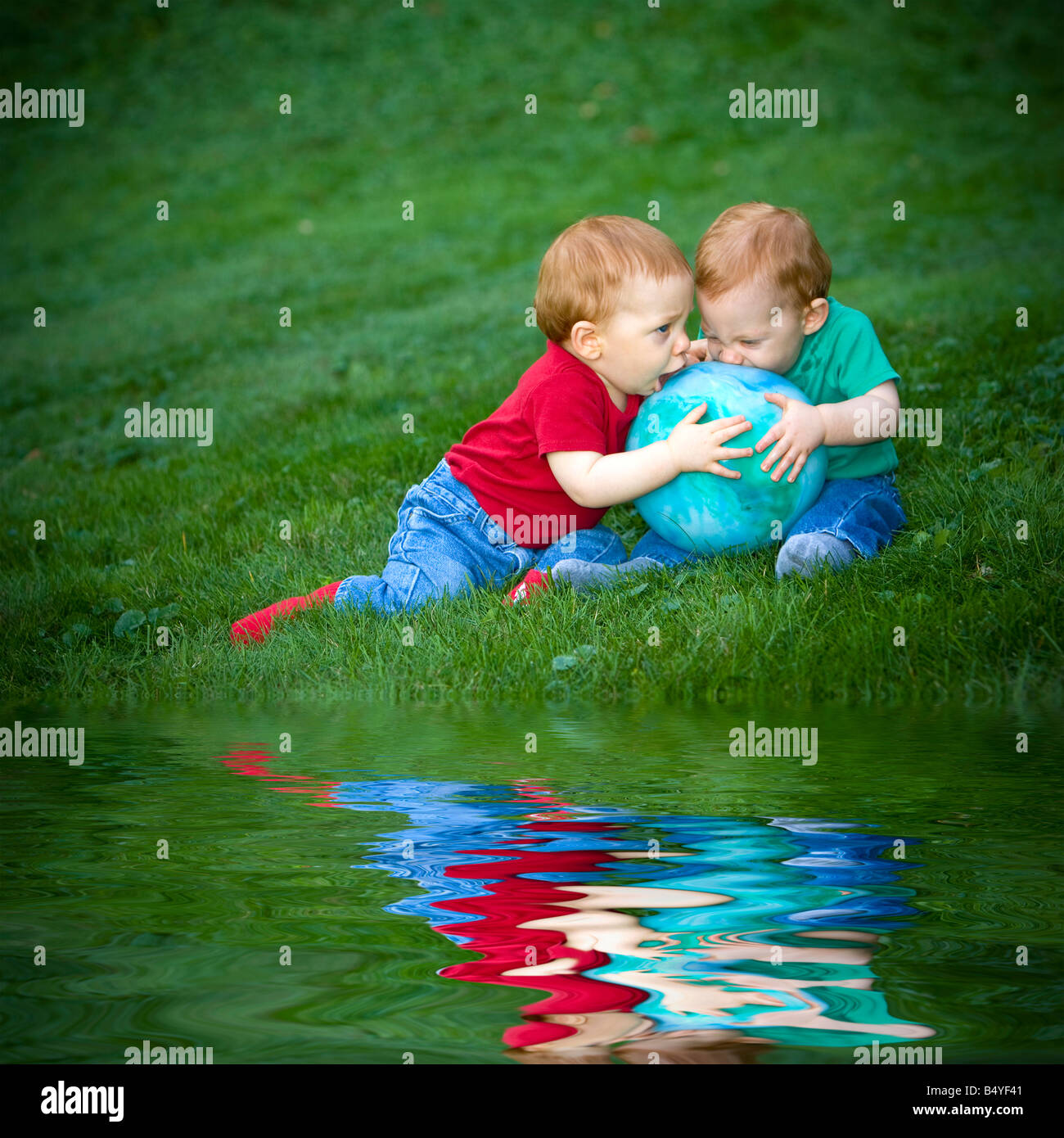 Giovani redheaded baby boys seduto fuori su erba giocando con sfera Foto Stock
