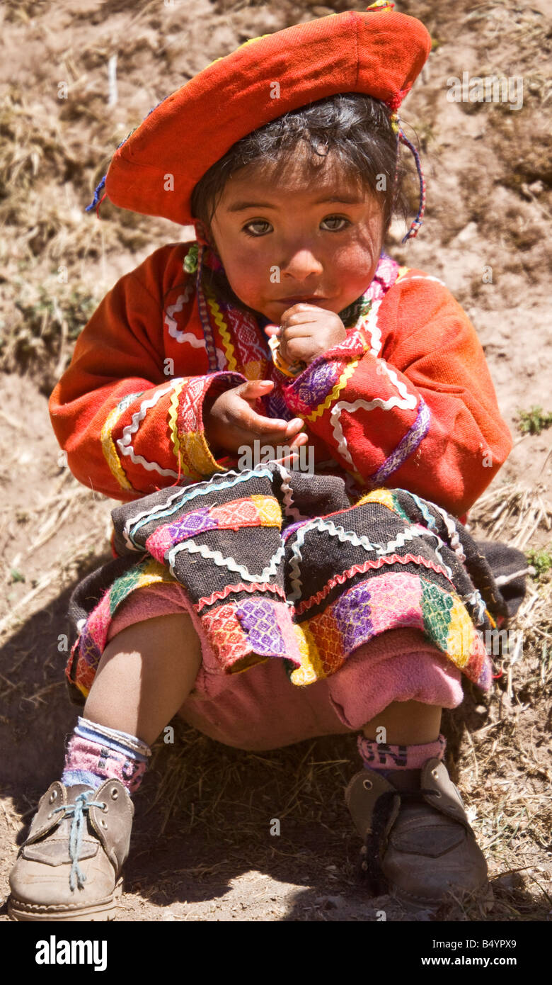 Piccola ragazza peruviana toddler indossando il tradizionale nativa nazionale costume andina o abiti tiene fuori la sua mano timidamente per un dolce. Foto Stock