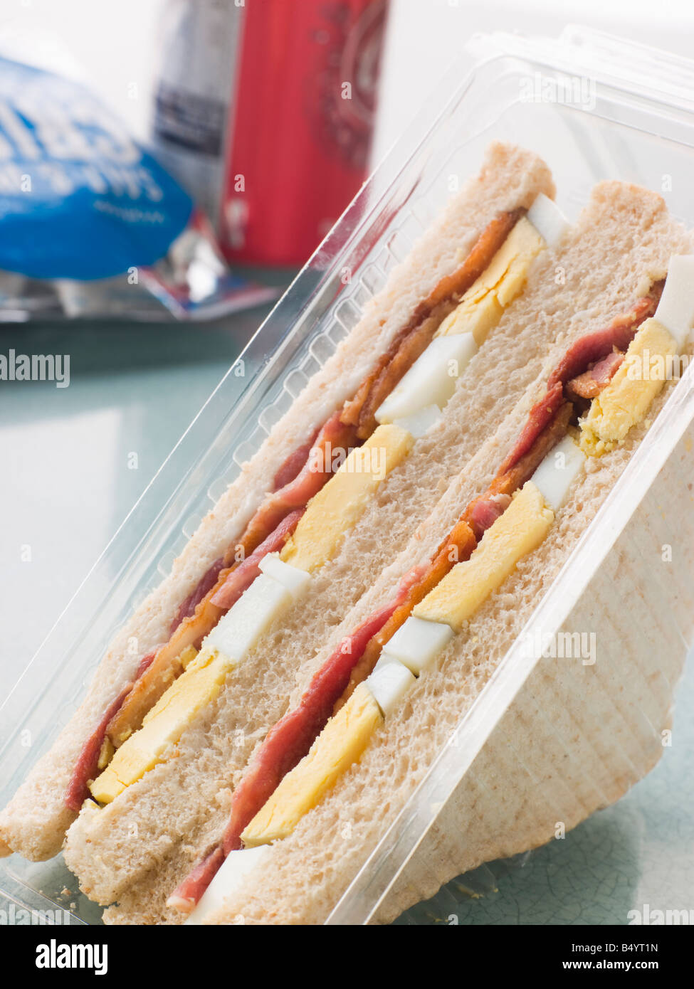 Uova e bacon in sandwich di pane bianco con un sacchetto di patatine e una lattina di bevanda frizzante Foto Stock