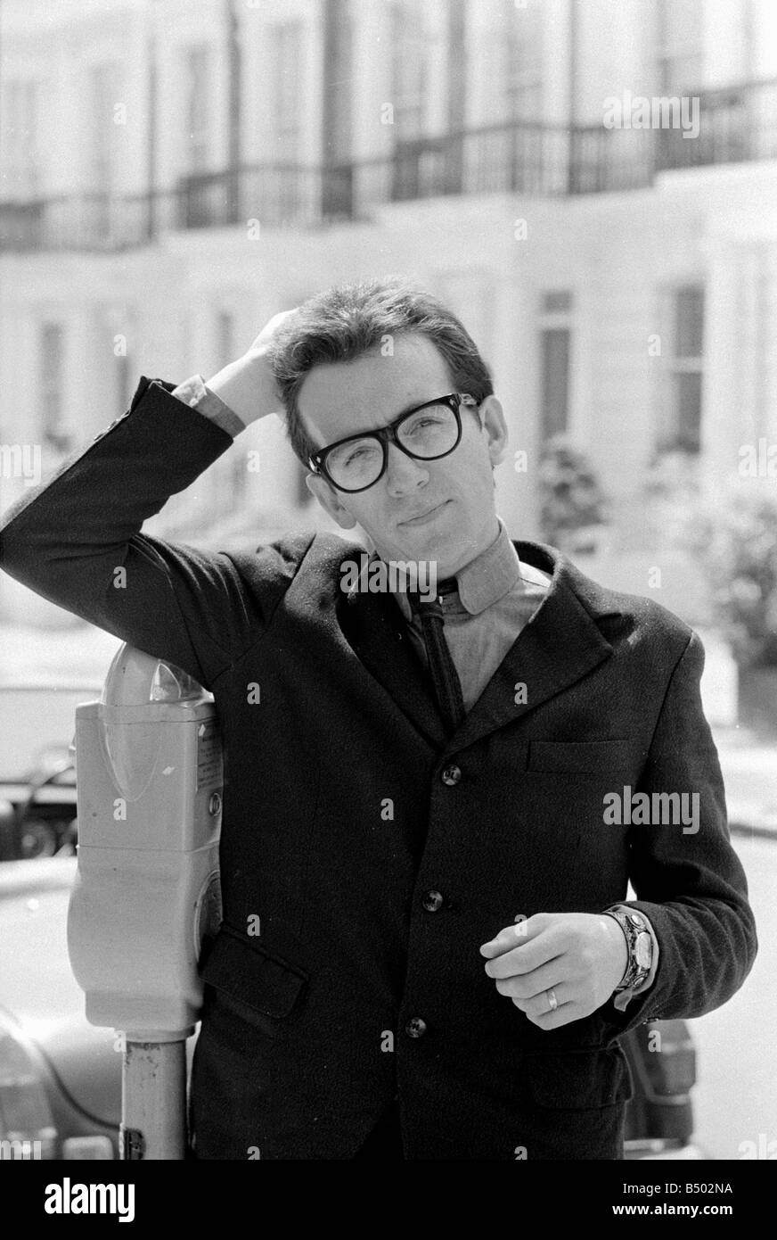 Elvis Costello la sensazione più recente sulla scena musicale in piedi accanto ad un parcheggio macchina bicchieri tenendo la mano sulla parte superiore della sua testa Agosto 1977 anni settanta Foto Stock