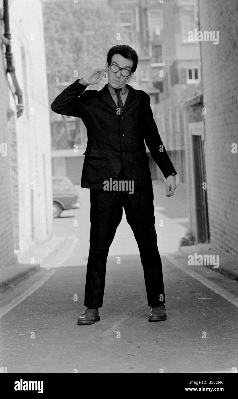 Elvis Costello la sensazione più recente sulla scena musicale in piedi nella piccola strada divertente pongono tenendo un dito nel orecchio la sua pulizia Foto Stock